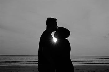 Silhouetted couple embracing by the beach at sunset, capturing a moment of romance. HD wallpaper