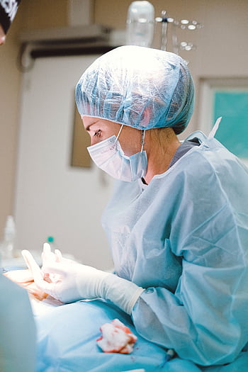 Female medical professional in surgical attire operating in a sterile room, focusing on patient care. HD phone wallpaper