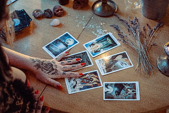 A mystical setup featuring tarot card reading on a wooden table, with artistic tattoos and dried flowers. HD wallpaper