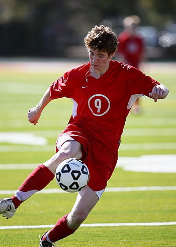 Soccer player in red uniform kicking ball during a match outdoors. HD phone wallpaper