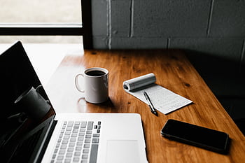 A tidy workspace featuring a laptop, coffee cup, , and notepad on a wooden desk. HD wallpaper