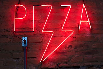 Vibrant red neon pizza sign glowing against a rustic brick wall at night. HD wallpaper