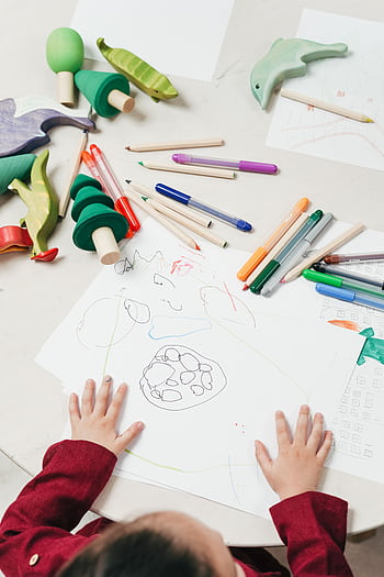 A child engages in creative drawing with colored pencils surrounded by wooden toys on a table. HD phone wallpaper