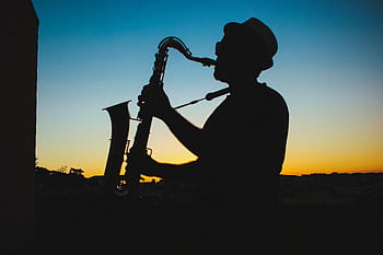 A man playing the saxo silhouetted against a vibrant sunset sky. HD wallpaper
