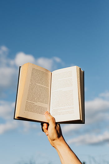 A hand holding an open book against a blue sky; symbolizes learning and dom. HD phone wallpaper