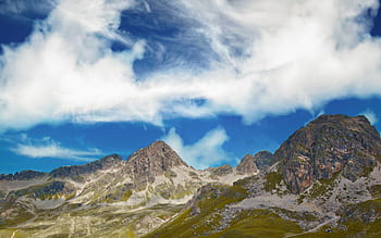 Explore the breathtaking beauty of rugged Alpine mountains under a vibrant blue sky with swirling clouds. HD wallpaper