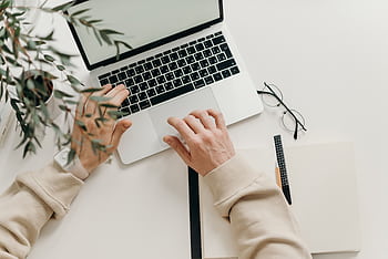 An overhead view of a person working on a laptop in a minimalist home office setting. HD wallpaper