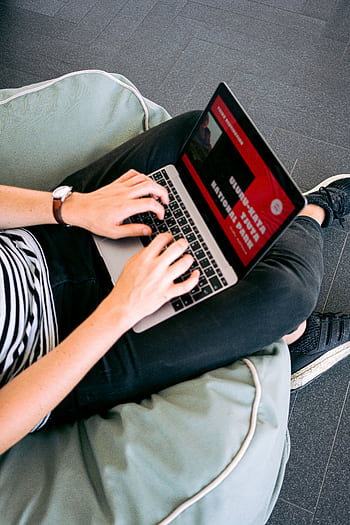 Person working remotely on a laptop while sitting comfortably on a beanbag chair indoors. HD phone wallpaper