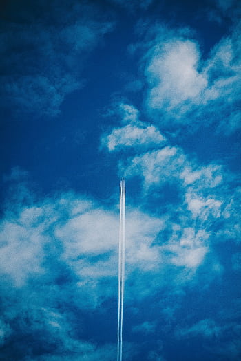 An airplane leaves a contrail across a bright blue sky filled with light clouds. HD phone wallpaper