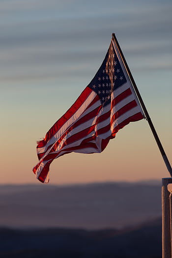 A vibrant US flag waves against a scenic sunset backdrop in Stowe, Vermont. HD phone wallpaper