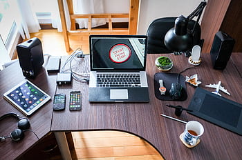 A contemporary office desk setup with laptops, gadgets, and accessories, creating a tech-savvy workplace. HD wallpaper