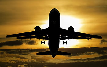 Silhouette of an airplane flying against a dramatic sunset sky. HD wallpaper