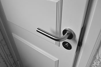 Close-up of a sleek steel door handle on a white door, showcasing modern interior design in monochrome. HD wallpaper
