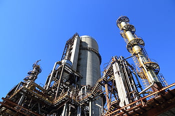 A towering industrial plant under a vivid blue sky, showcasing its intricate architecture and industrial prowess. HD wallpaper