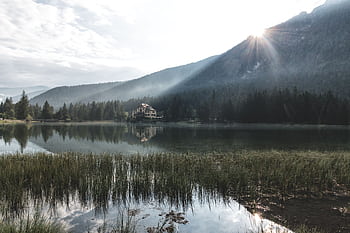 Peaceful lake view with house, mountains, and forest at sunrise. Tranquil and serene atmosphere. HD wallpaper