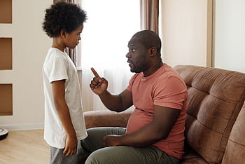 Father and son engaged in a heartfelt conversation on the sofa, illustrating parenting in a loving family setting. HD wallpaper