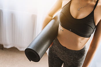 Fit woman in active wear holding yoga mat indoors, ready for workout. HD wallpaper