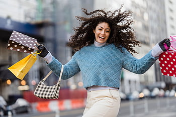 Cheerful woman enjoying a shopping spree outdoors in a city setting, showcasing vibrant lifestyle. HD wallpaper