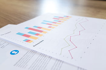 A close-up view of a business document with charts and graphs on a wooden desk. HD wallpaper