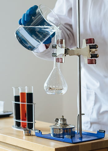 Scientist pouring liquid into a flask in a laboratory setting for research. HD phone wallpaper