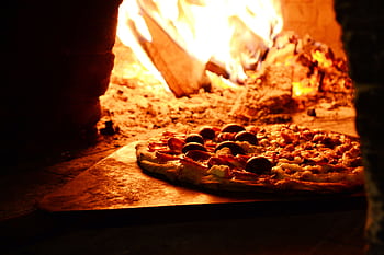 Delicious pizza baking in a traditional wood-fired oven with vibrant flames. HD wallpaper