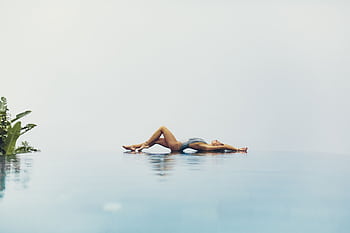 A woman relaxing by an infinity pool under a clear sky, reflecting serenity and summer vibes. HD wallpaper