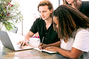 Young professionals collaborating on a project in a modern office with laptop and notes. HD wallpaper