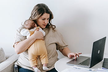 Mother multitasking with baby in arms and laptop at home office. HD wallpaper