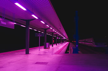 Explore the vibrant neon-lit train station platform in Toledo at night, showcasing urban architecture. HD wallpaper