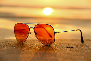 Close-up of sunglasses on a beach during a vibrant sunset, capturing the essence of summer. HD wallpaper