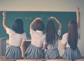 Group of teenage girls in school uniforms enjoying time together in a classroom, posing with playful gestures. HD wallpaper