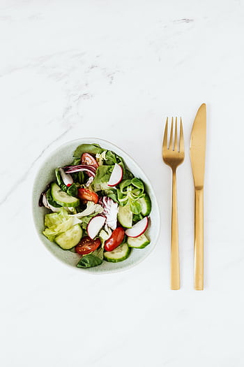 Bowl of fresh vegetable salad with golden cutlery on a marble surface, healthy meal concept. HD phone wallpaper