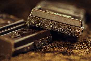 Macro shot of rich dark chocolate bars sprinkled with cocoa powder, highlighting texture and indulgence. HD wallpaper