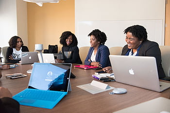 Group of women engaged in a collaborative meeting at an office table with laptops. HD wallpaper