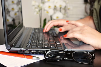 Close-up of a woman's hands typing on a laptop with glasses and a notepad on the desk. HD wallpaper