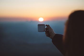A person holds a coffee cup against a beautiful sunrise, capturing a serene outdoor moment. HD wallpaper