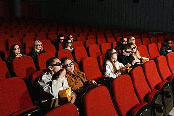 People in 3D glasses watching a movie in a theater with popcorn and red seats. HD wallpaper