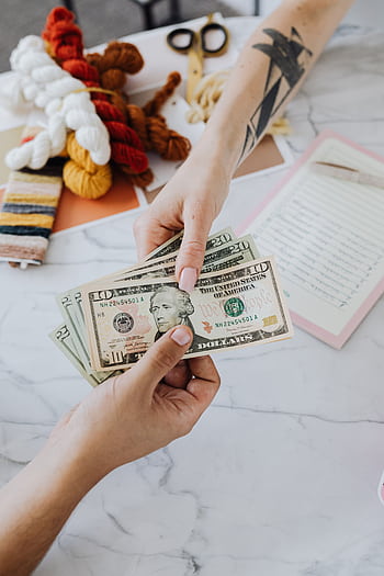 Hands exchanging US dollars on a table with crafting supplies, highlighting financial transactions. HD phone wallpaper