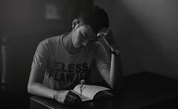Contemplative young man reading a notebook in a dimly lit room. HD wallpaper