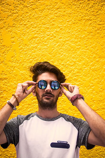 Young man with sunglasses standing against a vibrant yellow wall in daylight. HD phone wallpaper