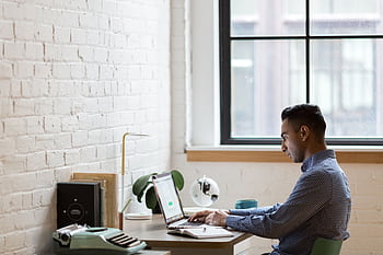 A focused businessman working on his laptop in a bright, modern office. HD wallpaper