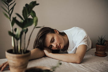A woman peacefully resting her head on a table surrounded by indoor plants. HD wallpaper