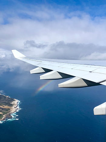 A scenic aerial view of an airplane wing over the ocean, featuring a rainbow in the sky. HD phone wallpaper
