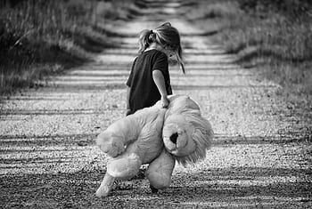 Monochrome of a child holding a teddy bear while walking down a dirt road, conveying a sense of solitude. HD wallpaper