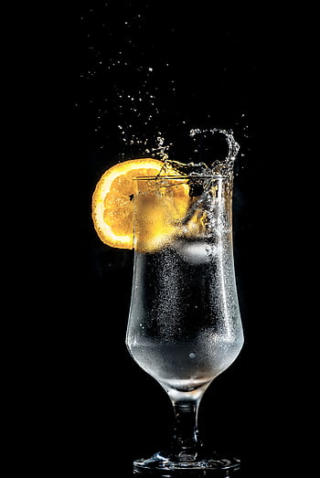 Dazzling cold cocktail with citrus slice splash, set against a dramatic black background. HD phone wallpaper