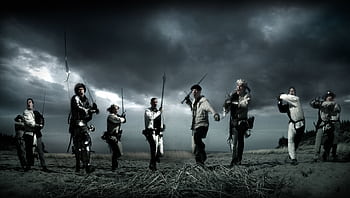 Dramatic scene of medieval knights charging in a reenactment battle under stormy skies. HD wallpaper