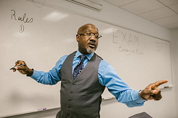 University professor energetically explaining exam rules in class. Academic atmosphere with focus on education. HD wallpaper