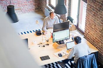 Bird's-eye view of a modern office with professionals collaborating on laptops and monitors. HD wallpaper