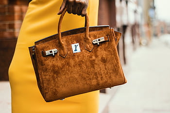 Chic brown leather handbag held by a fashionable woman in a vibrant cityscape. HD wallpaper