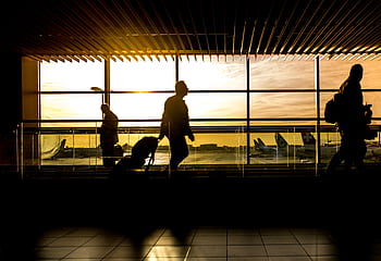 Travelers in silhouette pulling luggage at the airport during a beautiful sunset. HD wallpaper